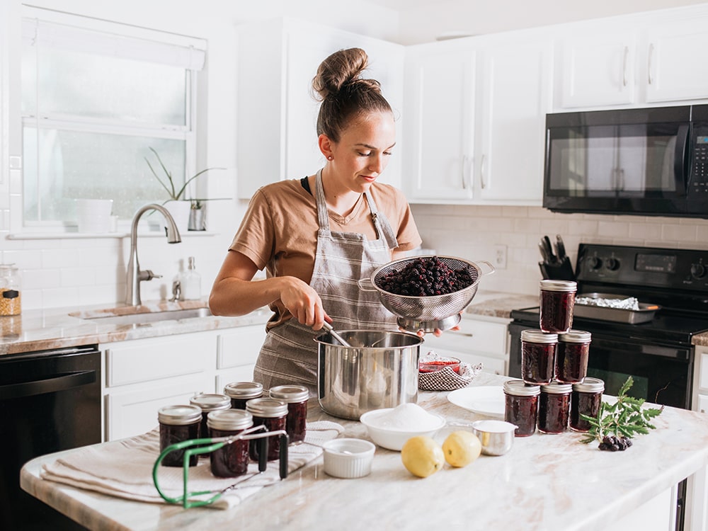 Woman canning homemade blackberry jam in home kitchen