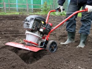 A person using a red rototiller from Wilco Farm store for seasonal garden preparation.