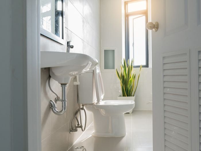 A white tiled bathroom with a white sink and white toilet.