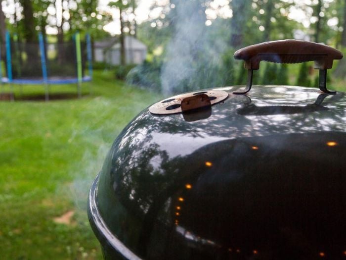 A charcoal grill with its cover on in a backyard.