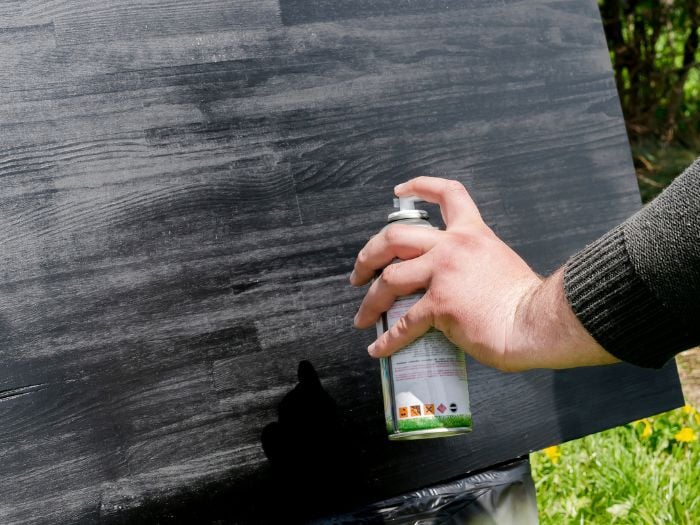 A person spay painting wood black.