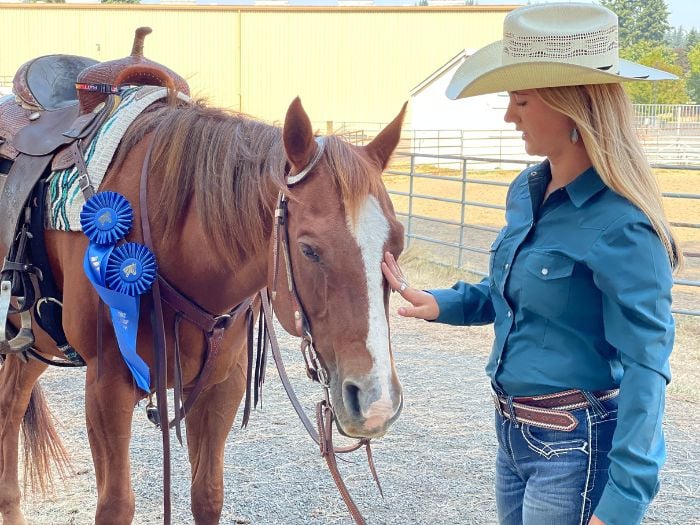 A western horse with several blue ribbons being pet by its rider.