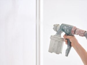 A person using a paint sprayer to paint a wall inside their home.