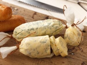 Cowboy butter rolled in a log and sliced on a cutting board next to bread.