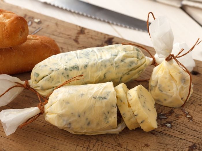Cowboy butter rolled in a log and sliced on a cutting board next to bread.