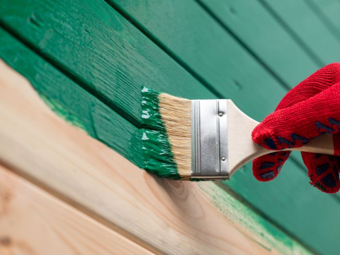 A person wearing a red glove painting an outside house wall green.